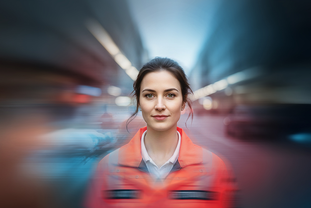 Notfallsanitäterin vor unscharfem Rettungswagen in Bewegung 